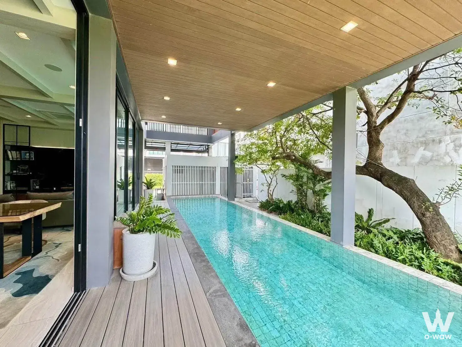 Covered outdoor pool area with wood deck and tropical plants in 4-bed condo for rent in The AVA Residence