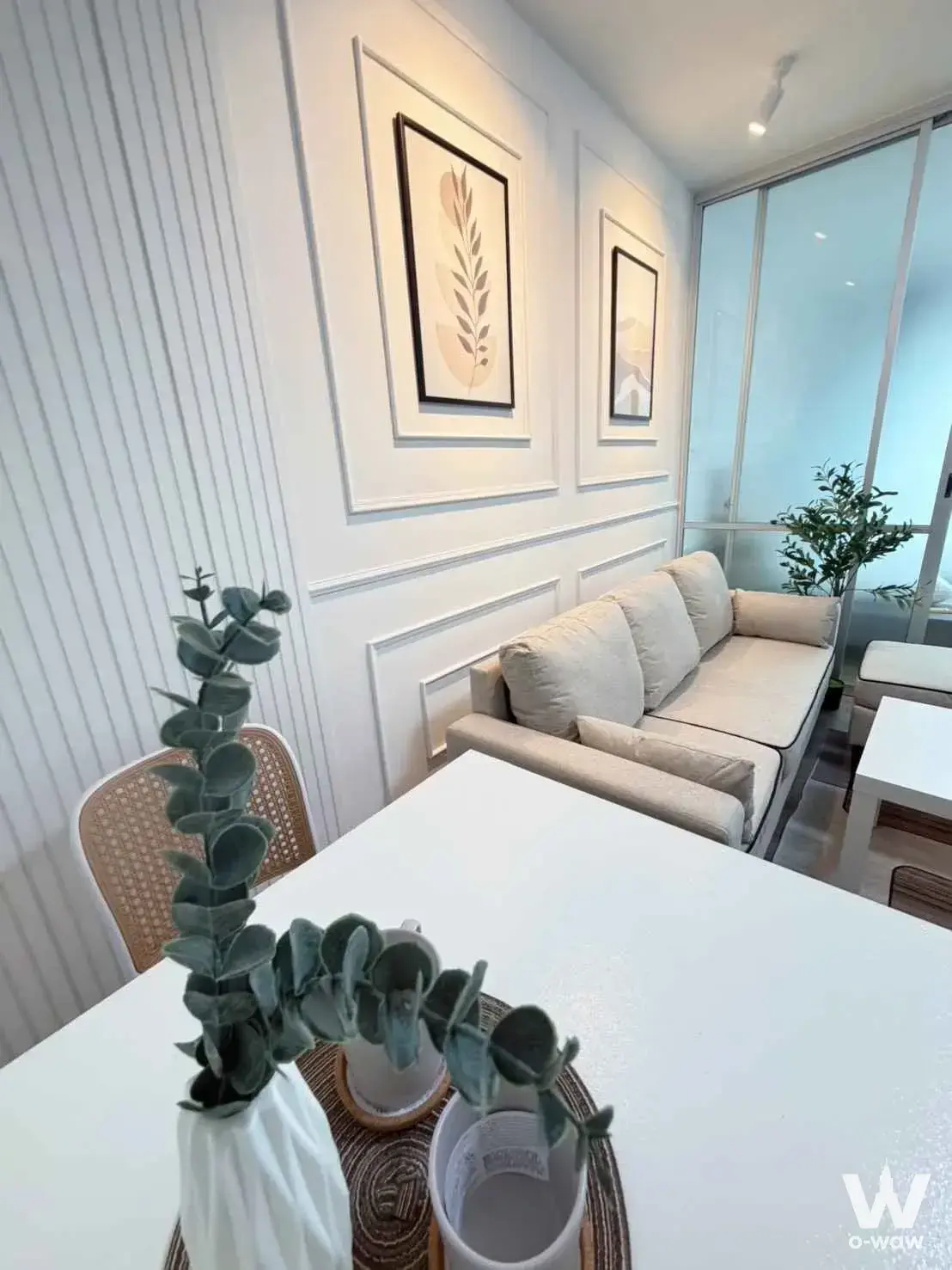 Modern 1-bed condo dining and living space featuring rattan chairs, fluted wall panels, and botanical prints at dcondo Creek