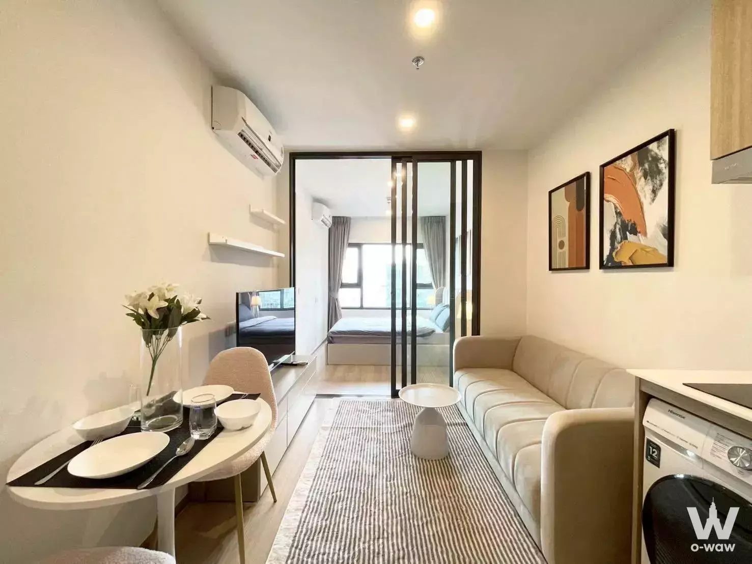 Bright open-plan living space with beige sofa, dining set, and built-in kitchenette in this Asoke condo for rent