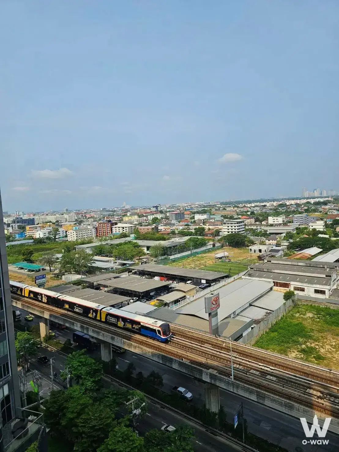 Elevated view of BTS train on tracks above busy road and urban landscape from Sukhumvit Eastgate condo balcony under blue sky