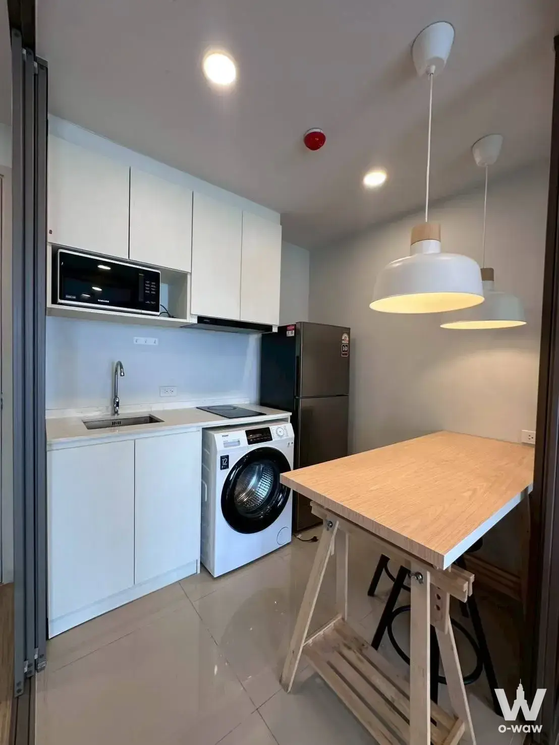 Compact kitchen with black induction cooktop and white cabinetry in ESQUE Condo Sukhumvit 101/1