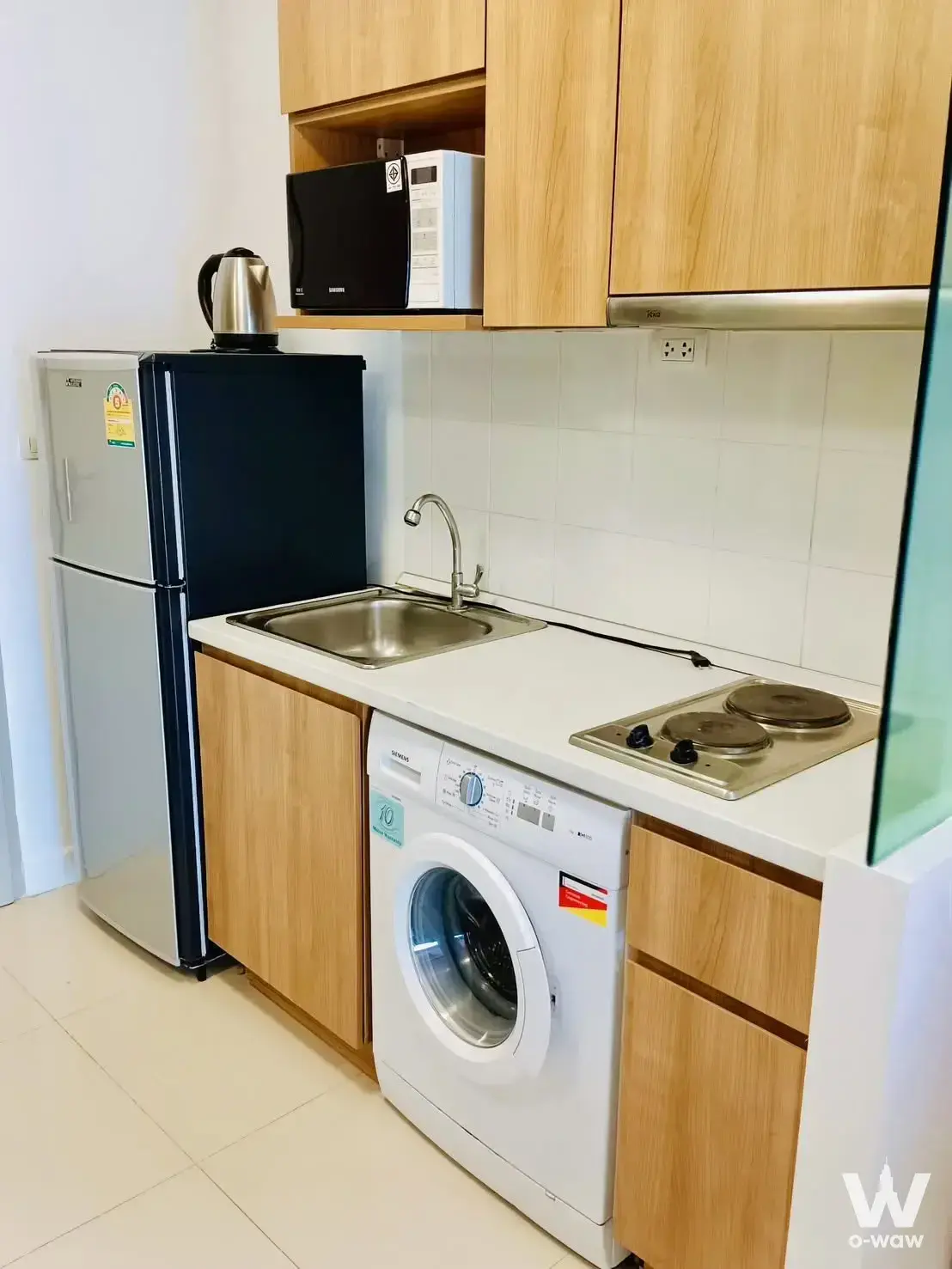 Compact kitchenette in Ideo Mix Sukhumvit 103 featuring light oak cabinets and built-in appliances