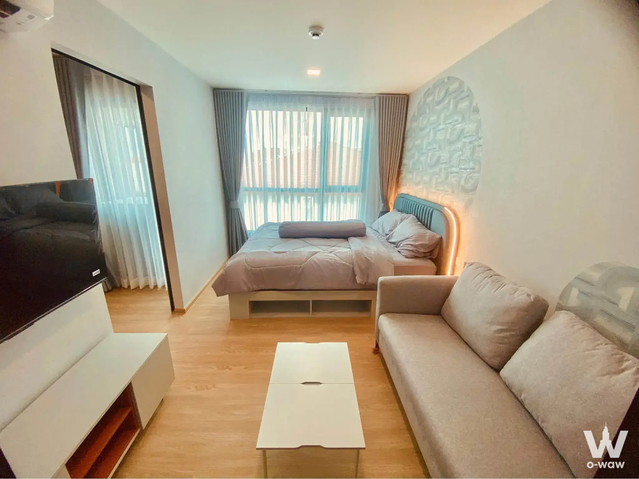 Open-plan living area with teal headboard, LED lighting, and large window in 1-bed Kave Luminous Bangmod