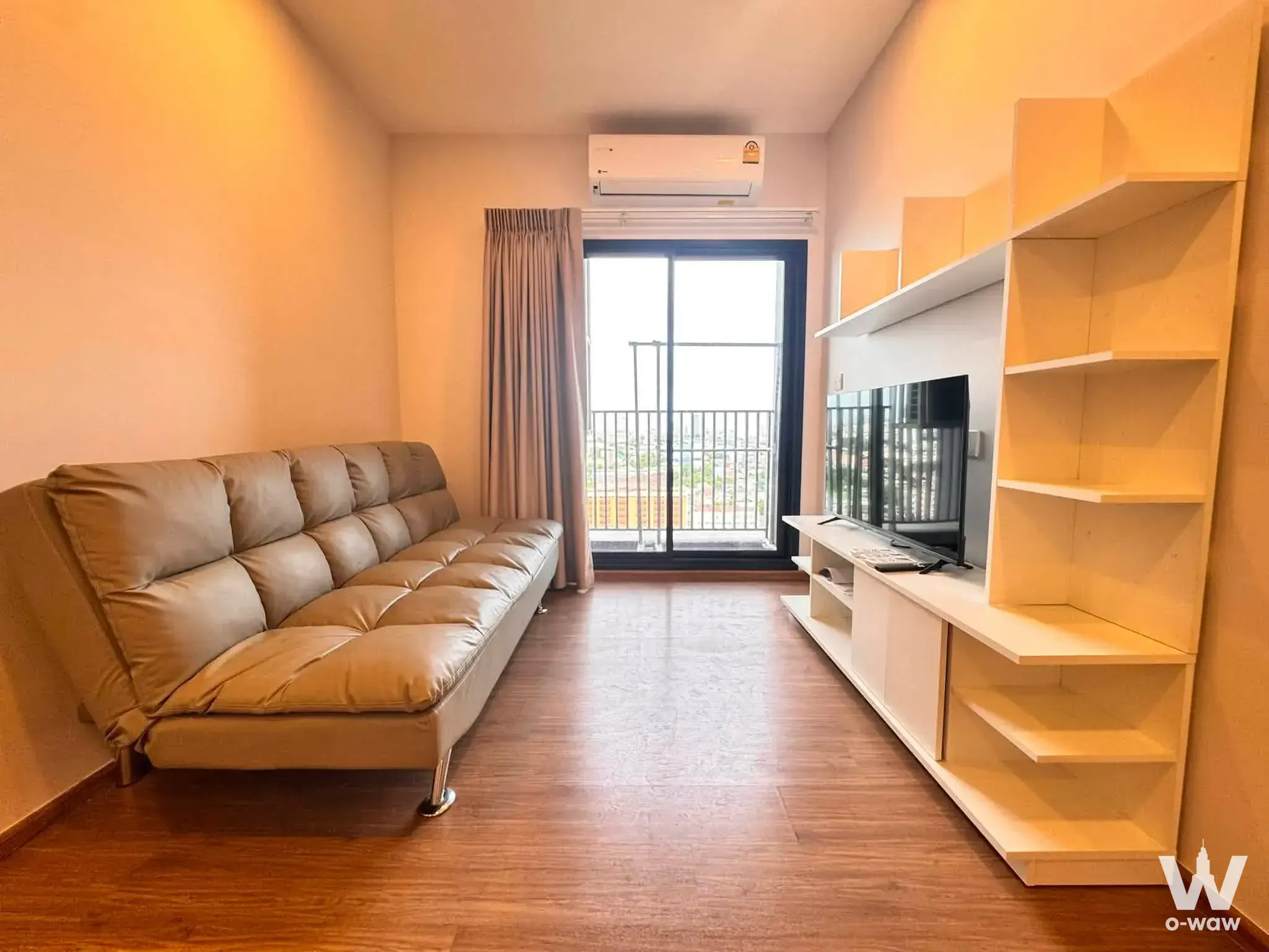 Living room in Metris Rama 9-Ramkumhang condo with beige sofa and built-in wood entertainment center