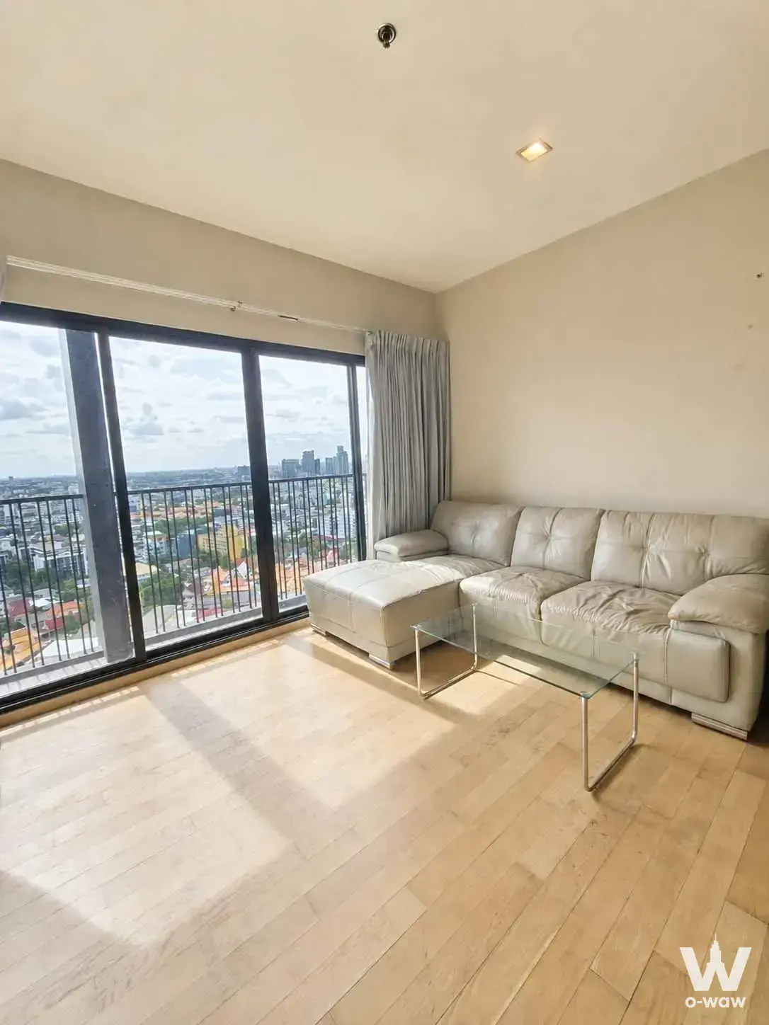 Bright living room in Noble Reveal with a beige leather sectional and floor-to-ceiling doors opening to a balcony