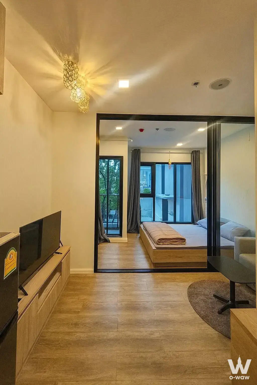 Open-plan 1-bed condo in Modiz Sukhumvit 50 with light wood floors and a sliding glass partition separating the bedroom