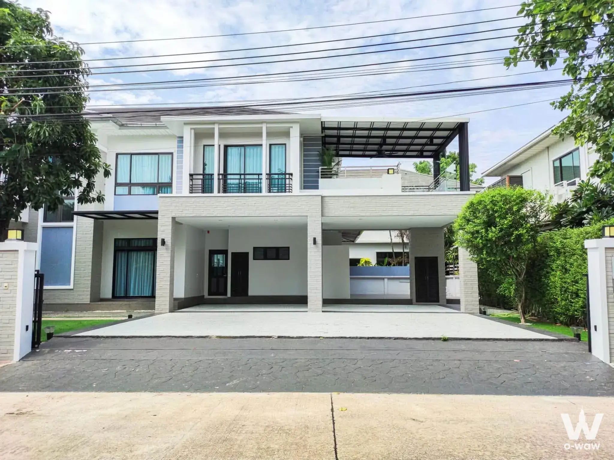 Modern two-story white house with grey brick accents, covered carport, and lush greenery