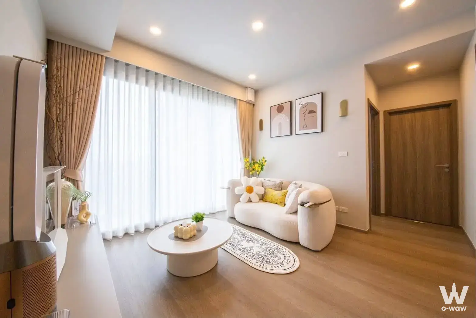 Living room in 2-bed Whizdom The Forestias condo with curved beige sofa, light wood floors, and floor-to-ceiling windows