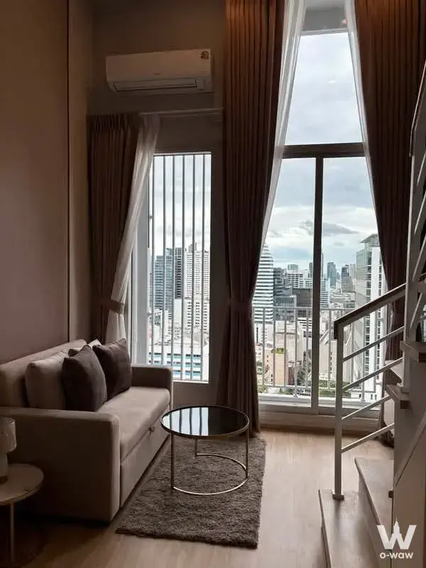 Beige sofa and city skyline view from a furnished 0-bed unit for rent in Culture Chula