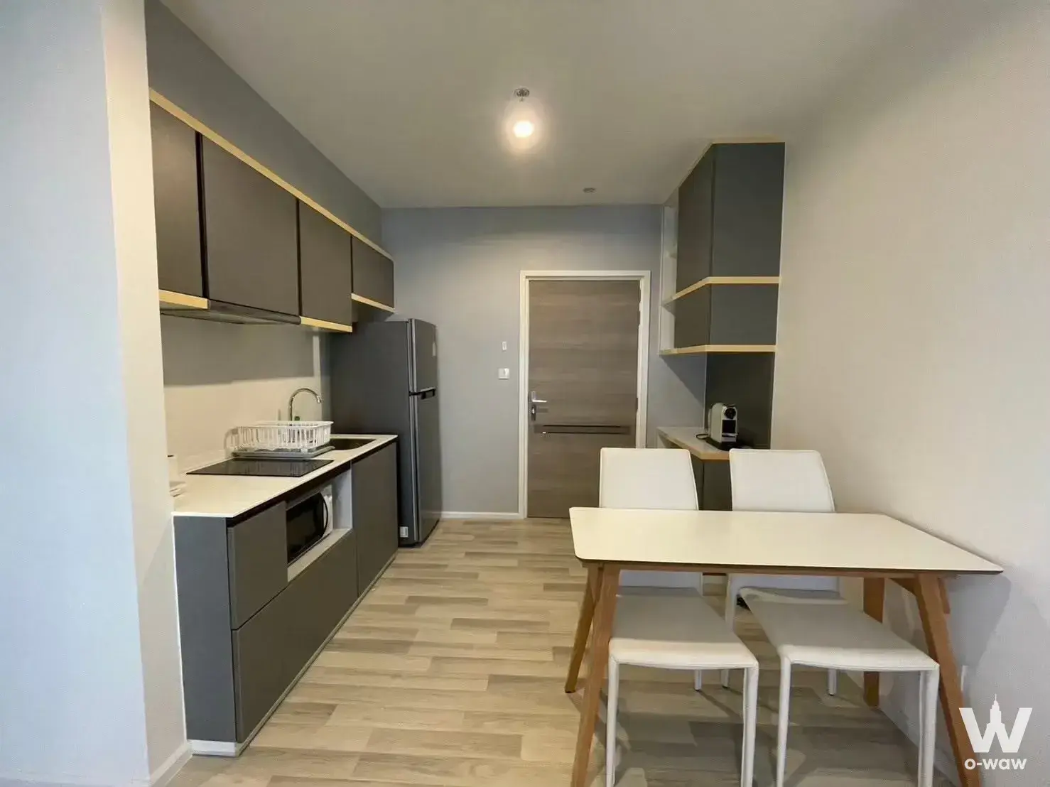 Open-plan kitchen in The Key Sathon-Charoen Rat condo with grey cabinets and a white dining table