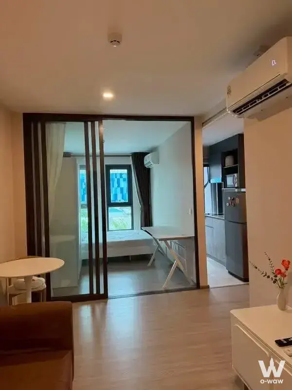 Living area in Aspire Ratchayothin 1-bed rental with leather sofa, glass partition, and open kitchenette