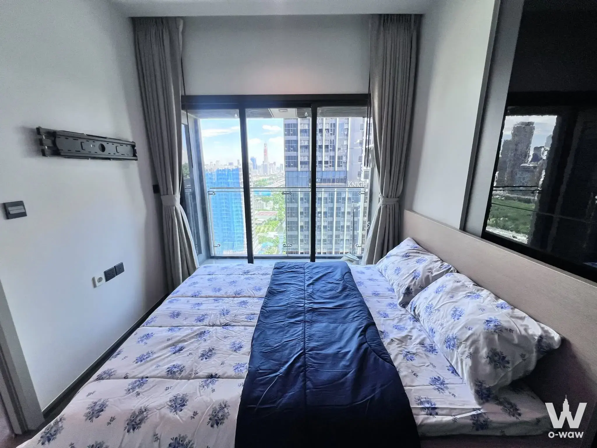 THE LINE Asoke-Ratchada 1-bed condo bedroom with blue floral bedding, balcony access, and city views
