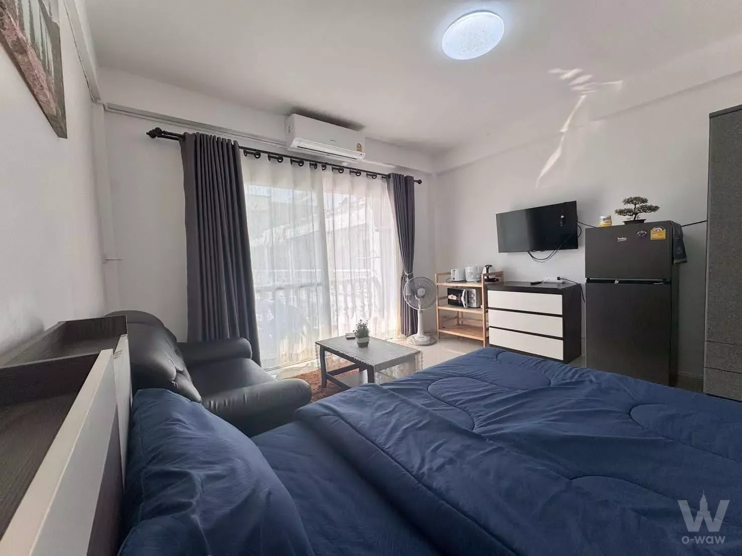 Studio bedroom in Majestic Jomtien condo with blue bedding, black sofa, and balcony access