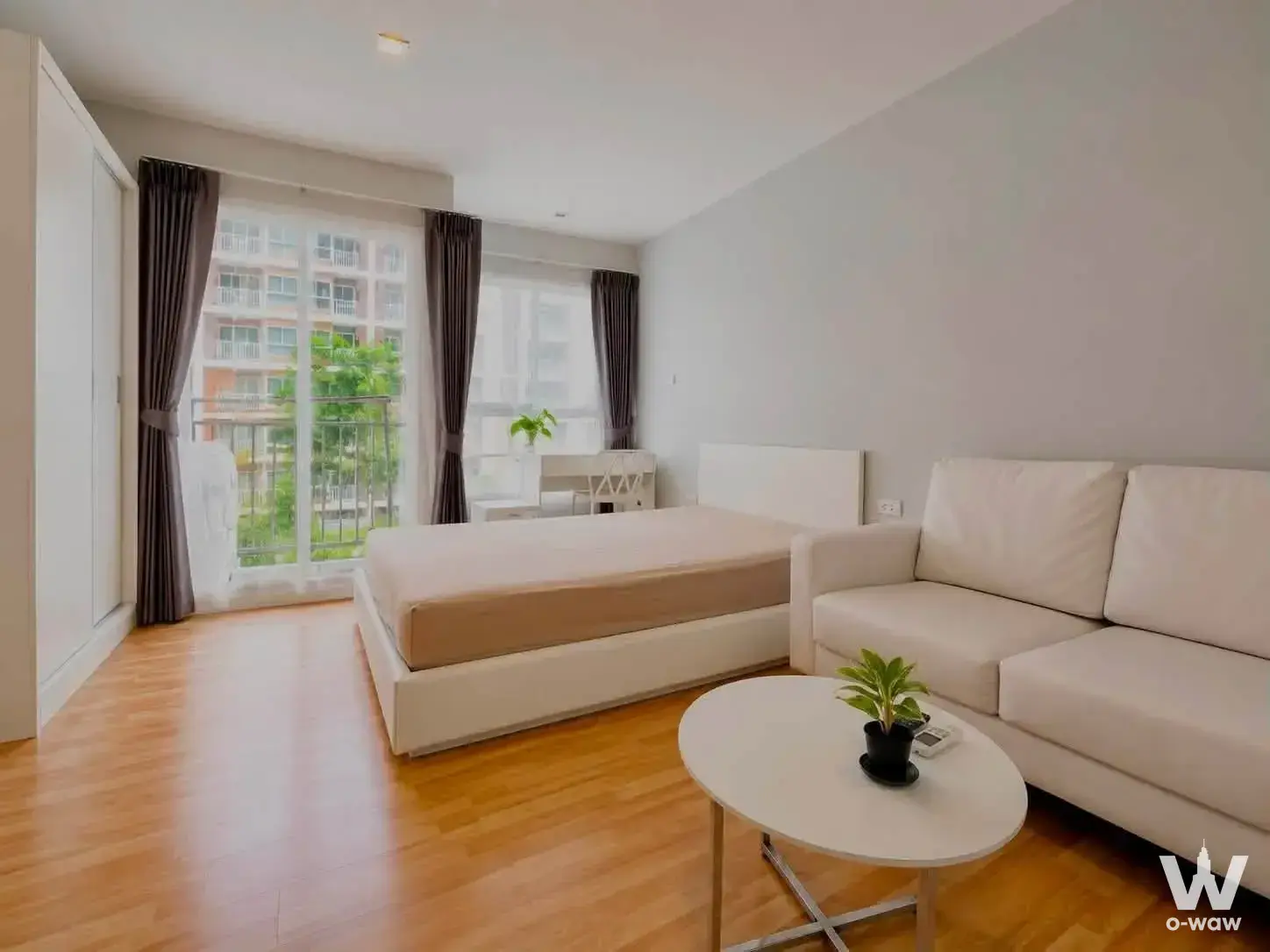 Open-plan studio layout in a DOLCE LA SALLE 1-bed condo featuring light oak flooring, white walls, and balcony access