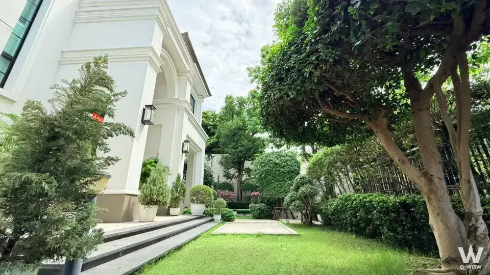 Luxury white stucco villa facade at Baan Sansiri Pattanakarn with arched entry, stone steps, and lush garden