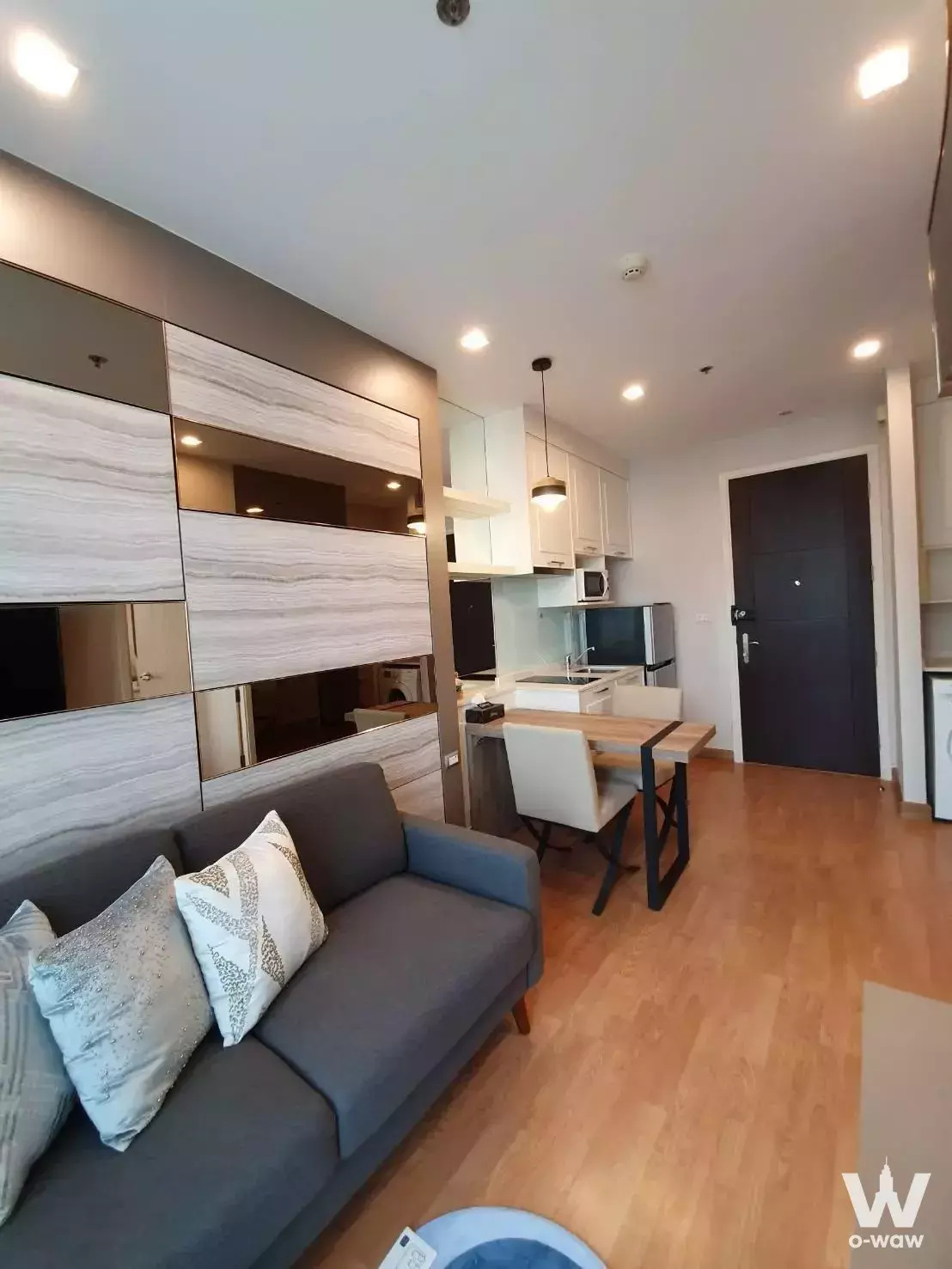Modern 1-bed condo living area with grey sofa, marble wall, and open kitchen in Q House Sukhumvit 79
