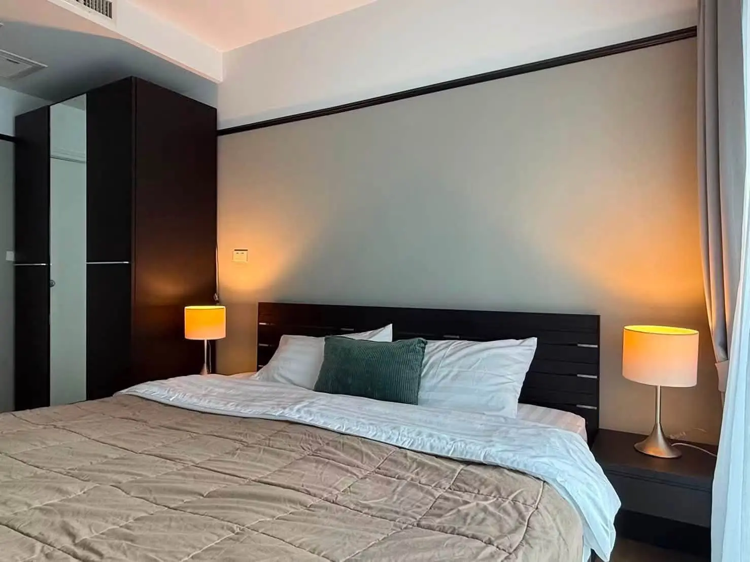 Master bedroom in a Noble Remix 1-bed condo featuring a dark wood bed frame and beige quilted comforter