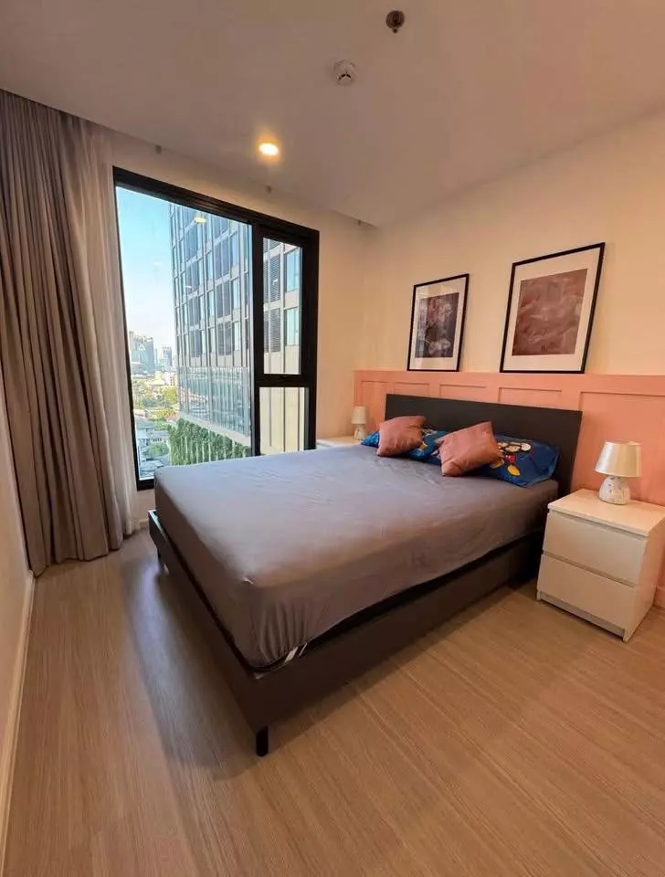 High-floor bedroom with salmon-pink accent wall and city view in DENIM Jatujak condo