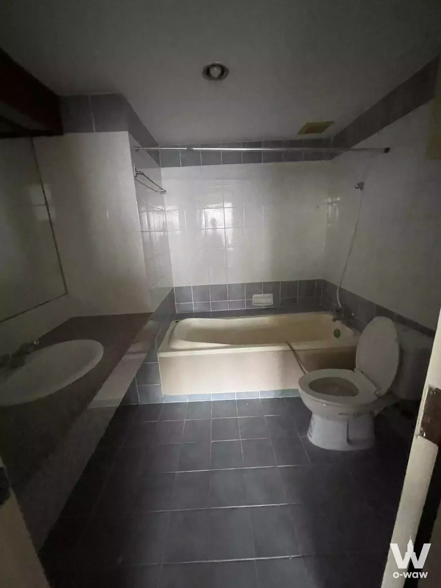 Ratchada Orchid condo bathroom featuring beige bathtub, dark grey tiles, white toilet, and long vanity