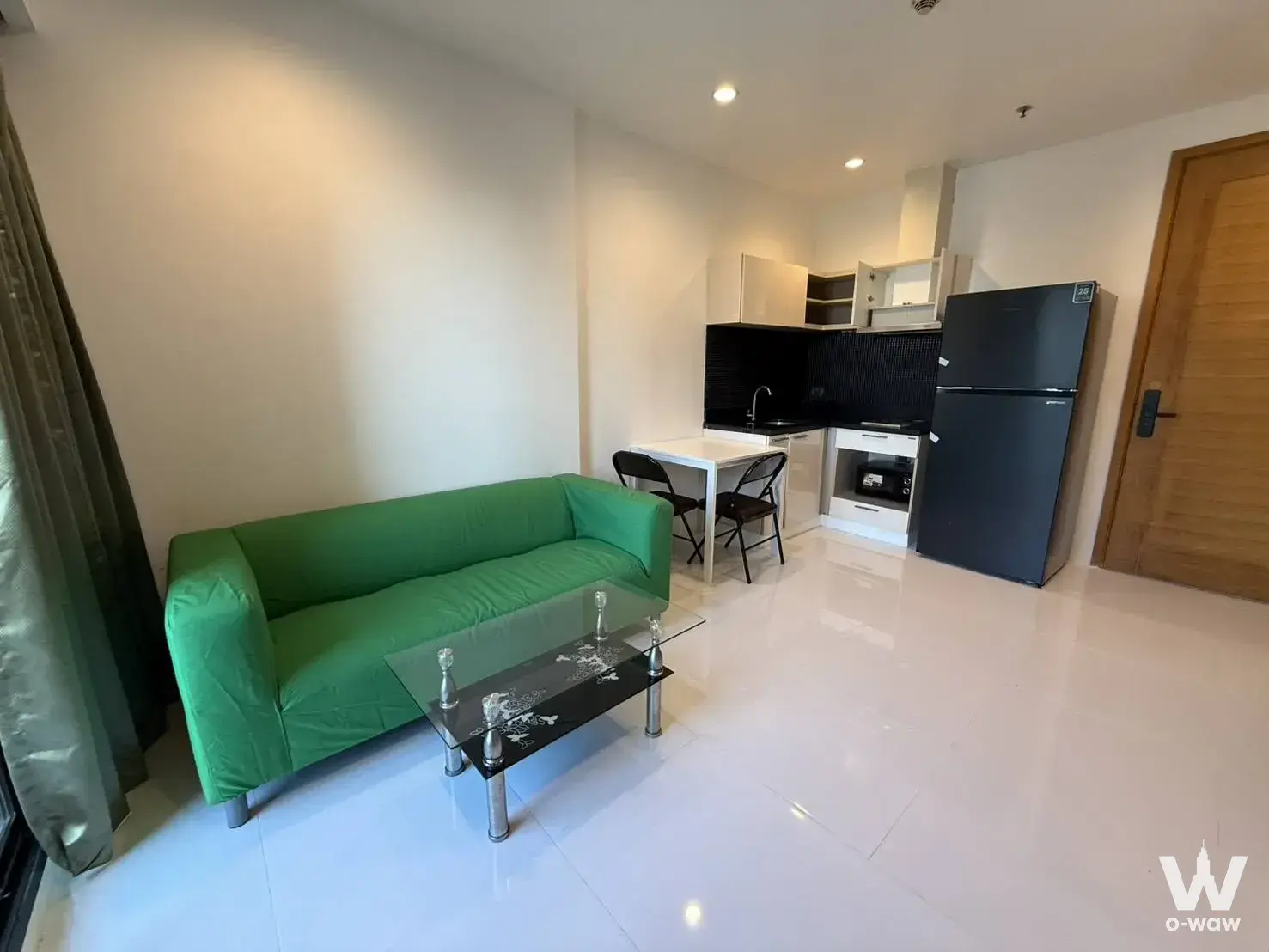 Bright studio in Fuse Sathon-Taksin featuring green sofa, glass coffee table and compact white kitchenette