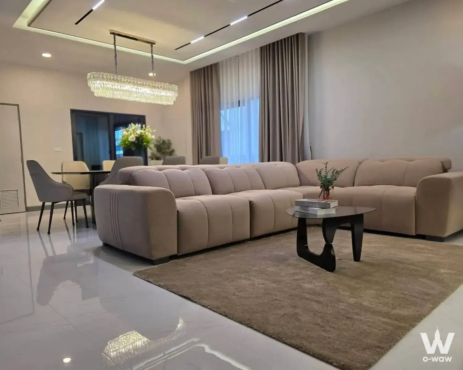 The living room in a 4-bed house for rent in The City Bangna KM.7 has a beige sectional sofa and crystal chandelier