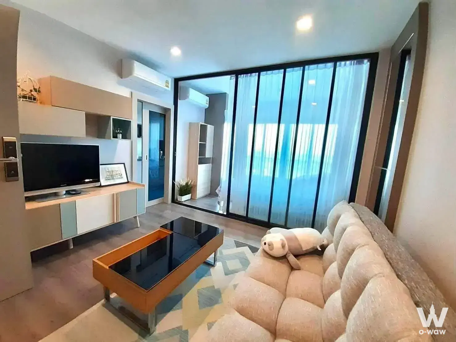 Living room in The Politan Rive for sale with beige sofa, glass coffee table, and sliding doors to an adjacent space