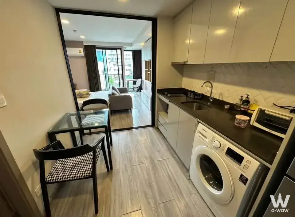 Open-plan kitchenette in Maestro 14 Siam-Ratchathewi with white cabinets and a view into the bedroom through sliding doors