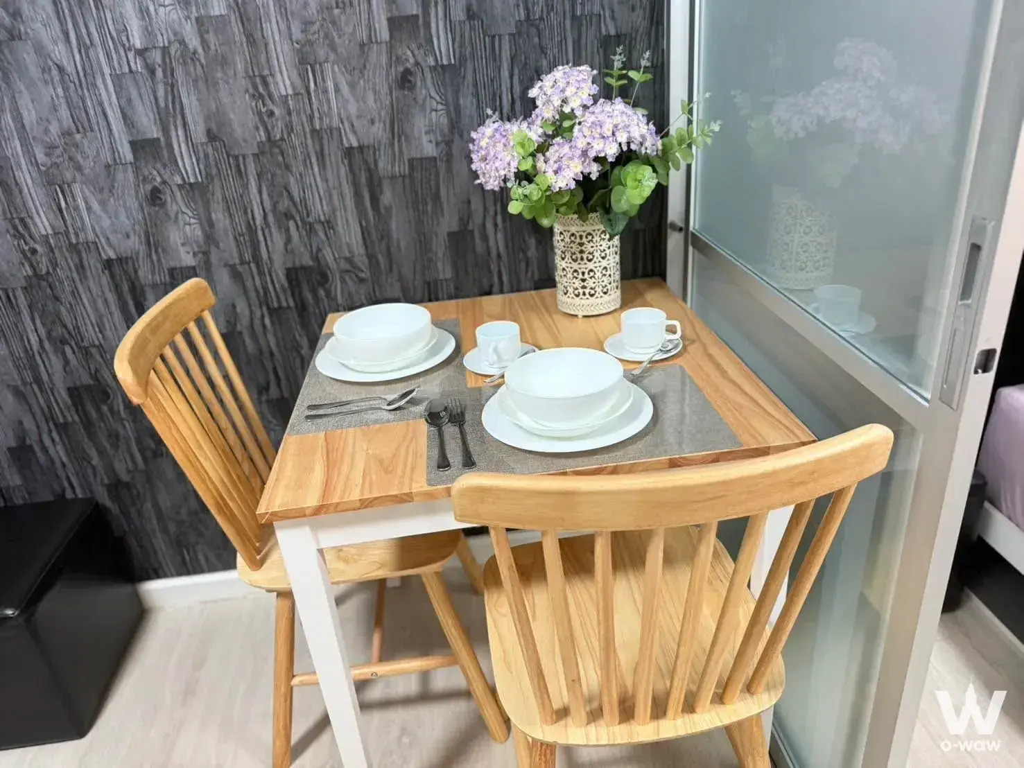 Compact dining nook in dcondo Sign Chiangmai with oak table, spindle chairs, and purple hydrangea vase against grey wall