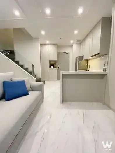 Living room with blue pillow and open kitchen island in 1-bed condo for sale at Ideo Q Phaya Thai