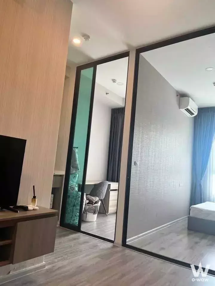Minimalist condo living area with walnut TV console and sliding glass doors to bedroom in KnightsBridge Collage Ramkhamhaeng