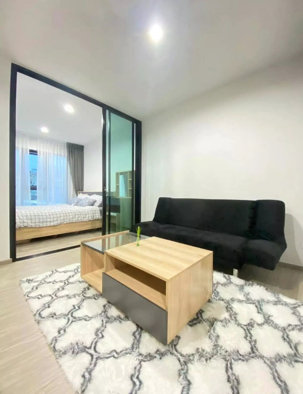 Minimalist 1-bed condo studio in RYE Sukhumvit 101/1 with black sofa, oak coffee table, and glass-partitioned bedroom