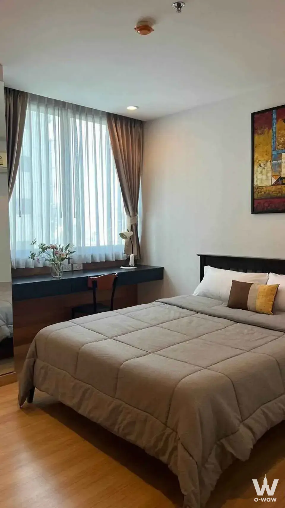 A queen bed and large window fill a bedroom in a neutral 2-bed condo for sale at The Rajdamri Serviced Residence