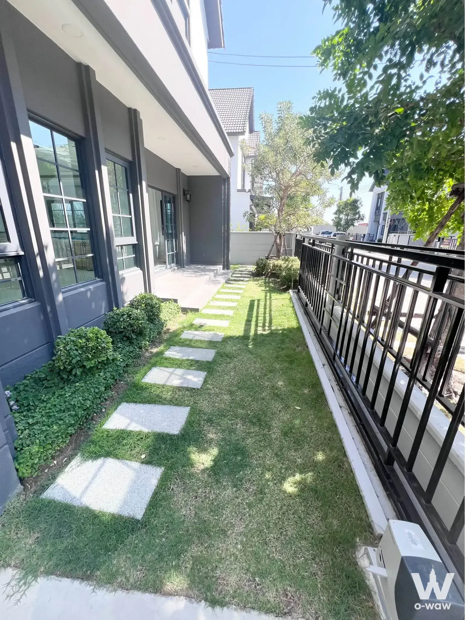 Side yard of 4-bed house for rent in Centro Bangna with stone pavers, shrubs, and black metal fence