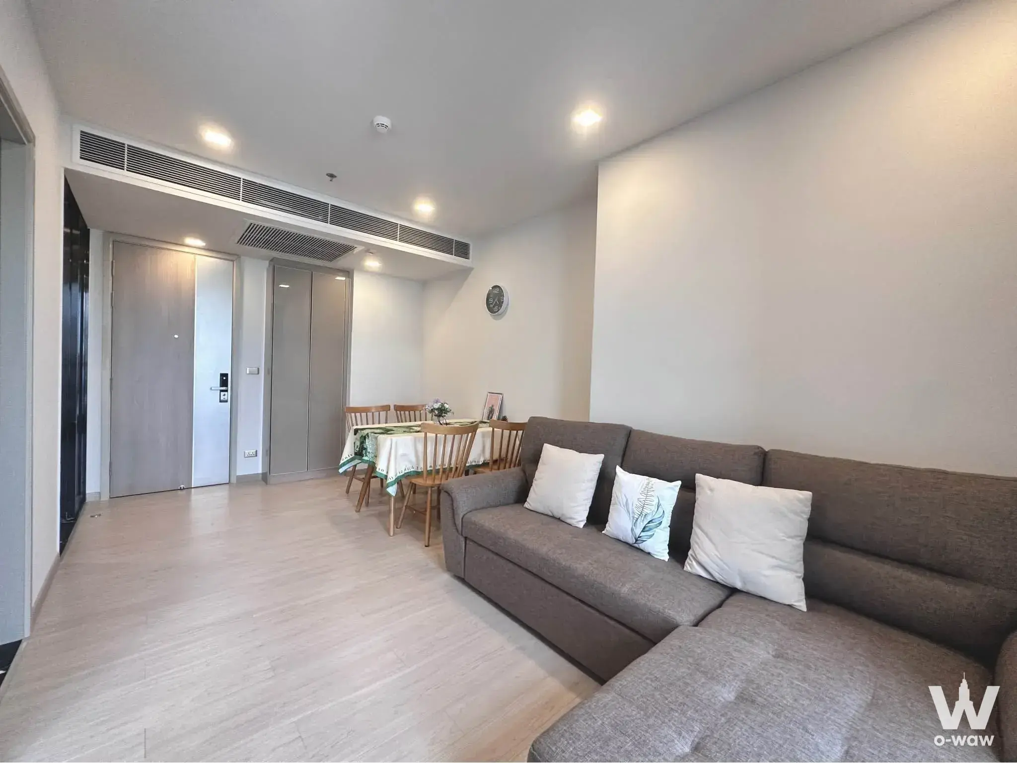 Spacious living area in a 1-bed rental at One9Five Asoke with grey sectional sofa and dining table set for four