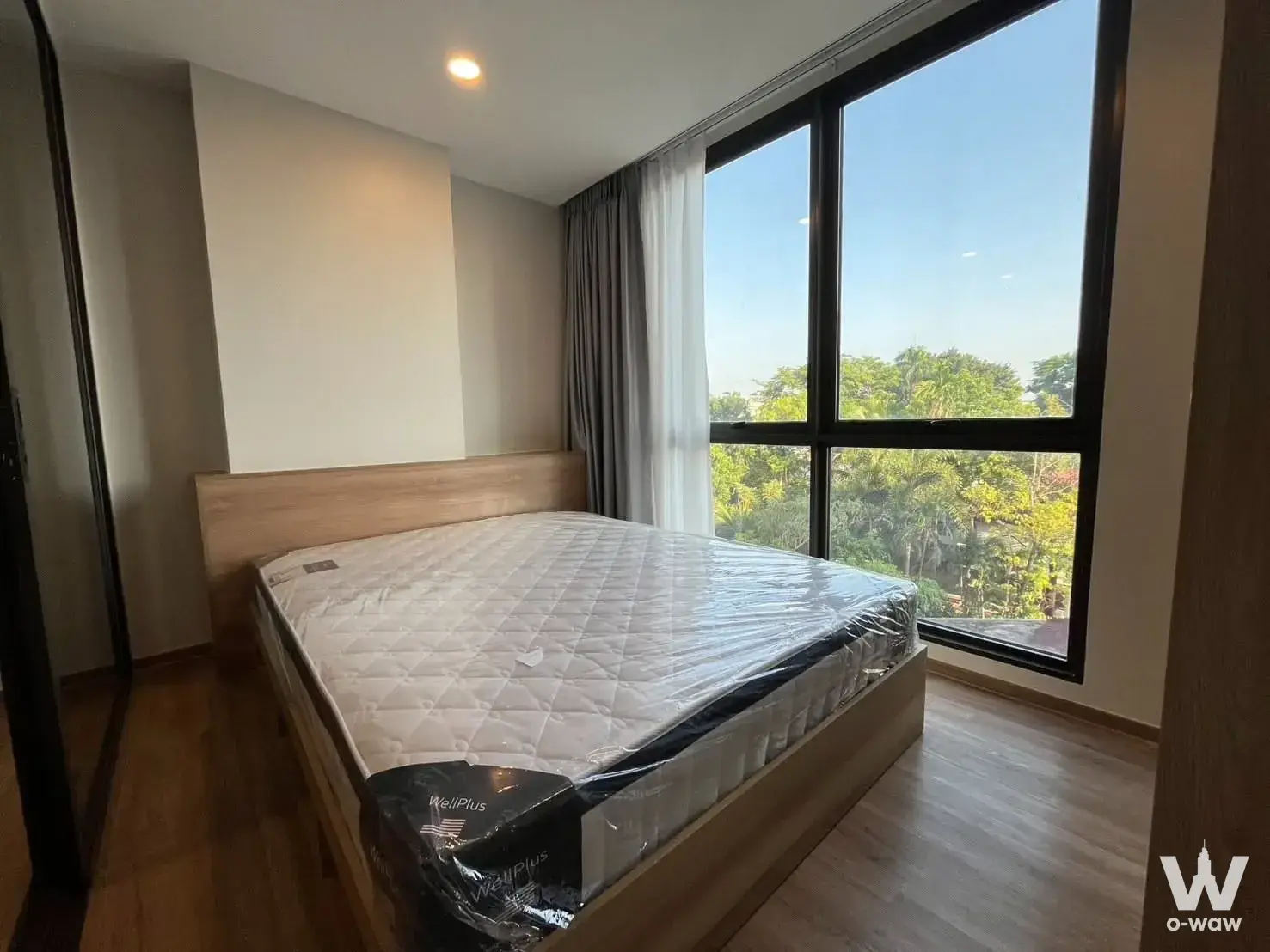 Bright bedroom for sale in Cybiq Rama IX featuring light wood bed, window view, and minimalist design