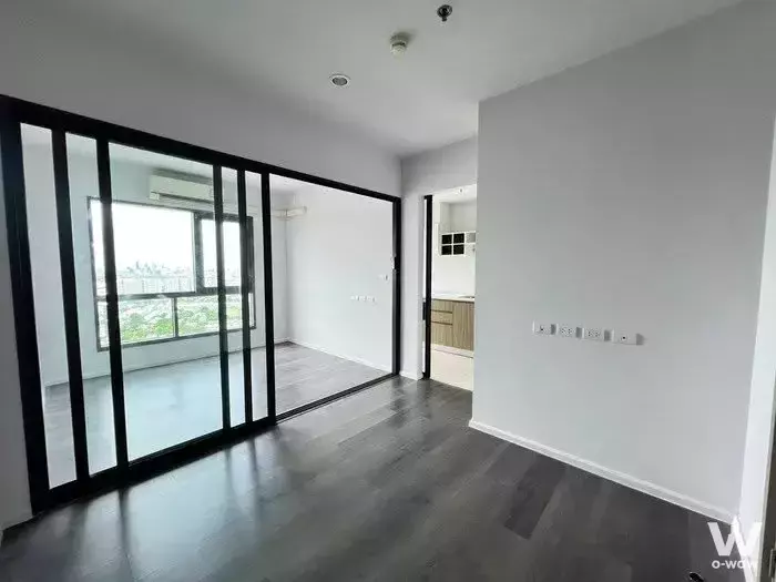 Empty living room with dark grey flooring and black-framed glass partition in 1-bed condo for sale at The Stage Taopoon