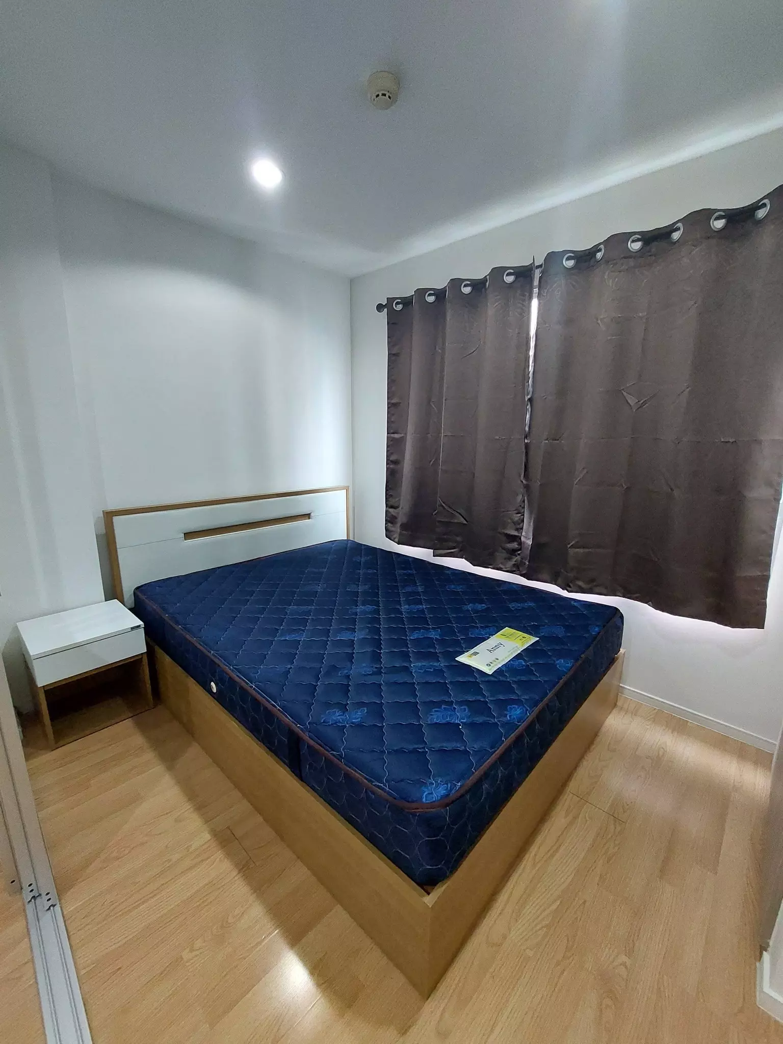 Bedroom in Lumpini Ville On Nut with wooden platform bed, blue mattress, and white nightstand