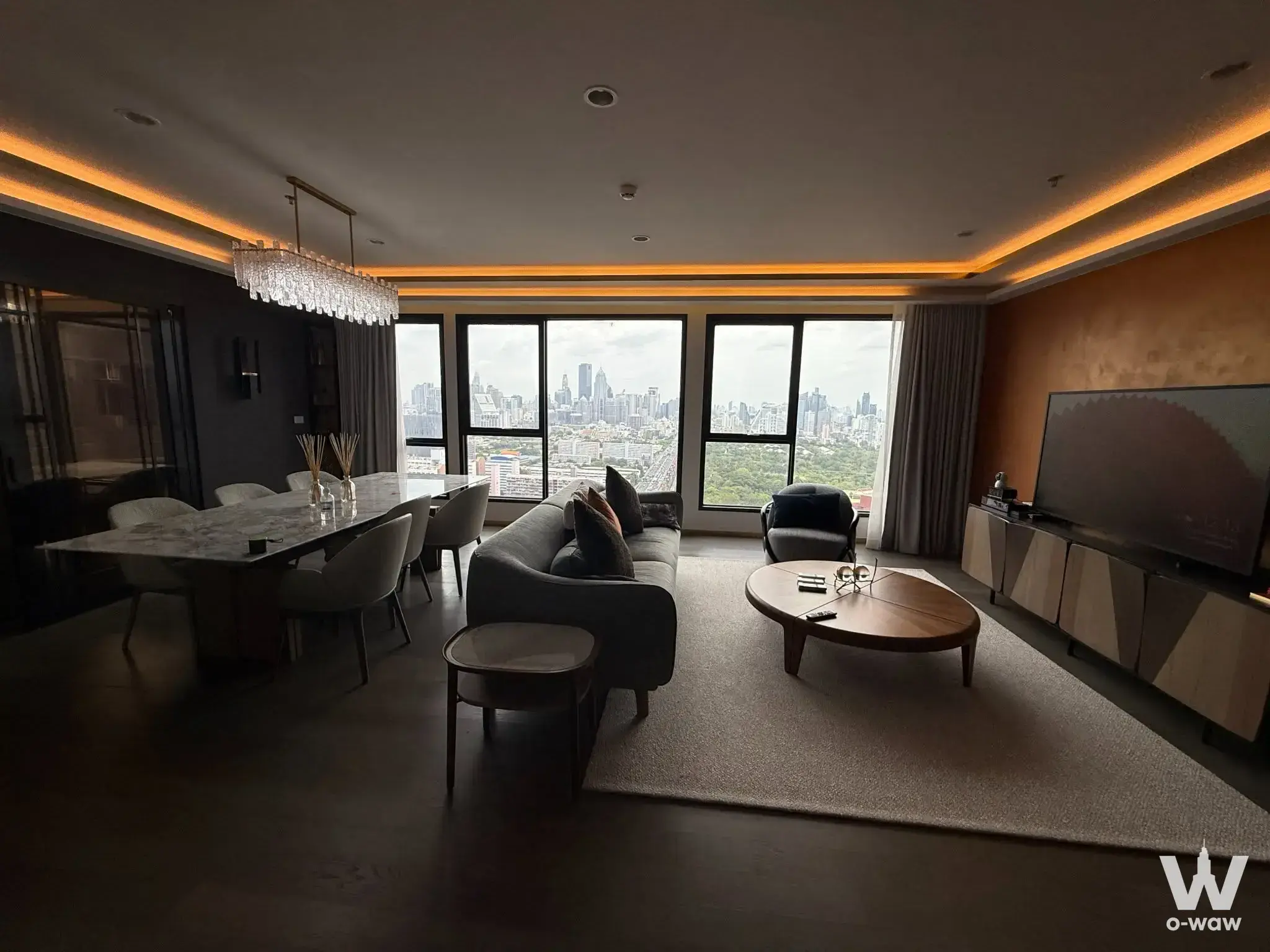 Spacious high-rise living room with city skyline views, crystal chandelier, and marble dining table