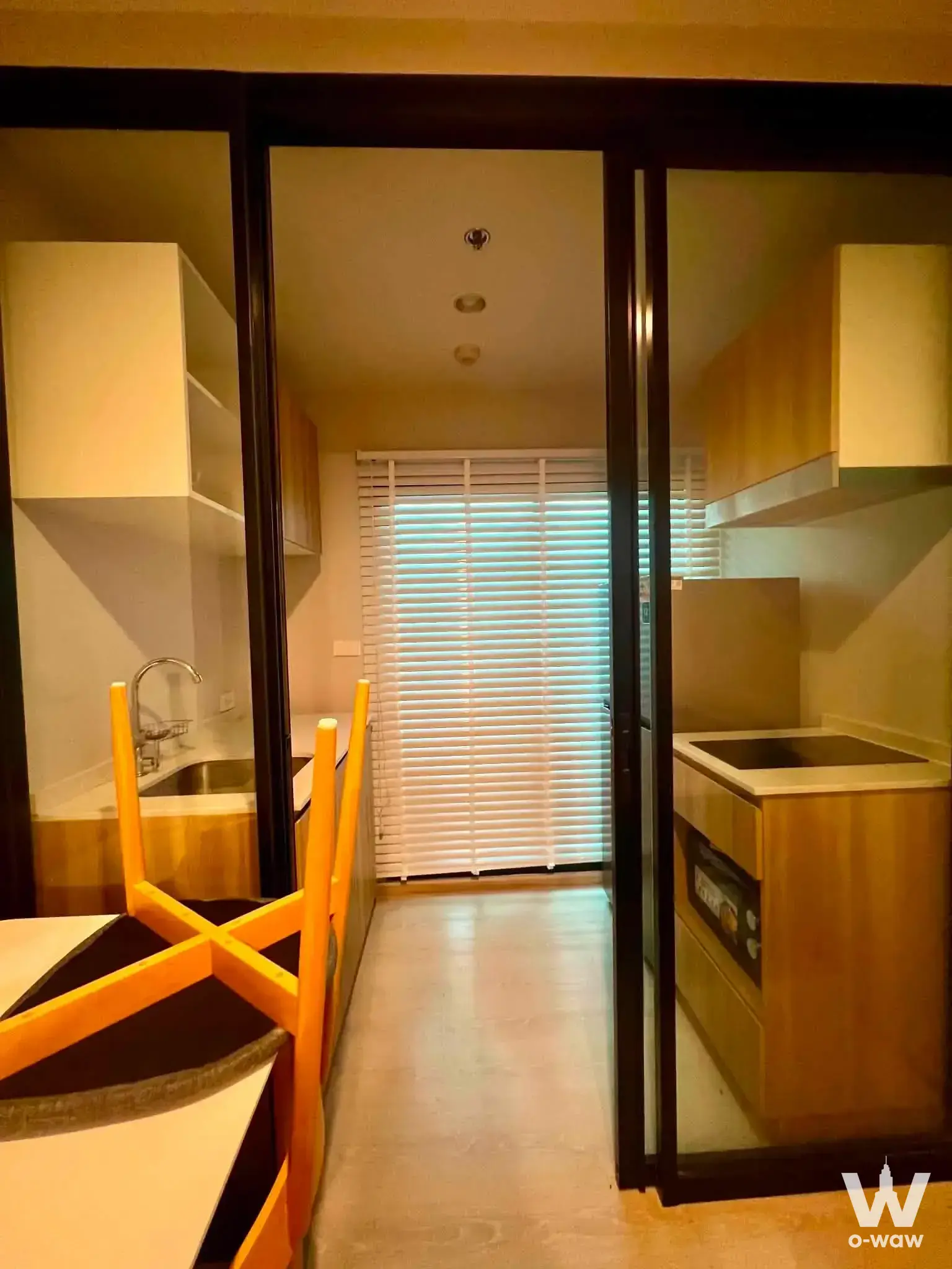 Compact galley kitchen with black sliding doors and light wood cabinets in a 1-bed rental at Nue Connex Don Mueang