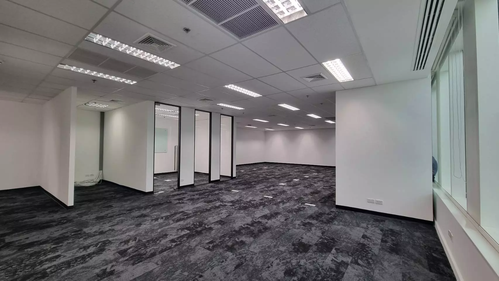 Empty open-plan office space in INTERCHANGE 21 with dark grey carpet tiles and glass-walled meeting rooms
