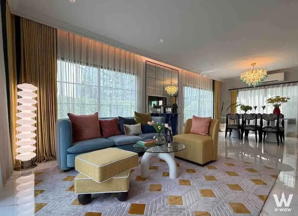 Open-plan living area in a Setthasiri Bangna-Suvarnabhumi home featuring a blue sofa, gold drapes, and floor-to-ceiling