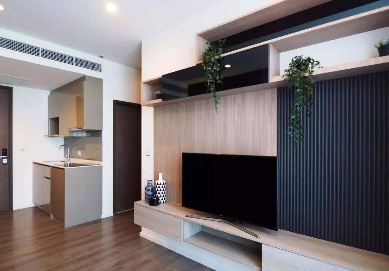 Open-plan living space with oak media wall, fluted paneling, and kitchenette in Whizdom Essence Sukhumvit 2-bed unit