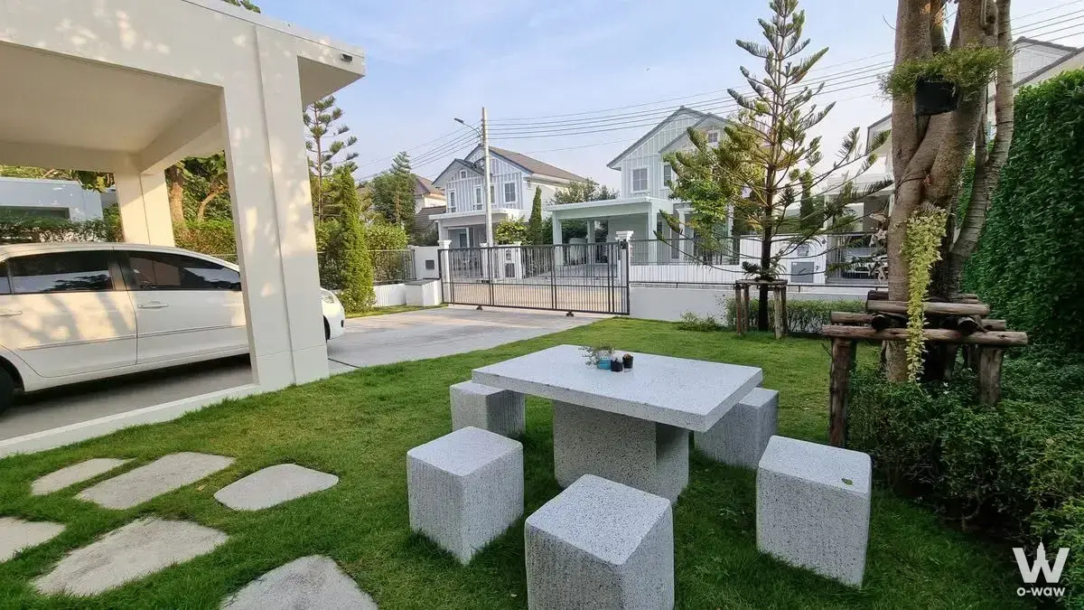 Front yard of house for rent in Villaggio 2 with manicured lawn, stone path, granite dining set, and carport