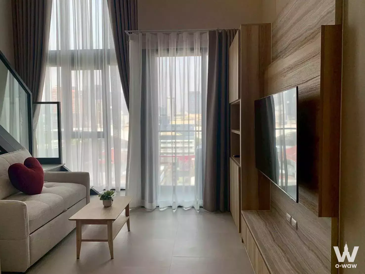 Cozy living room in Cooper Siam condo with grey sofa, wood paneling, and floor-to-ceiling windows