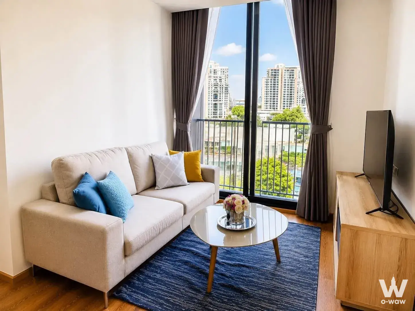 Noble BE33 1-bed condo living room featuring beige sofa, oak TV console, and bright balcony access