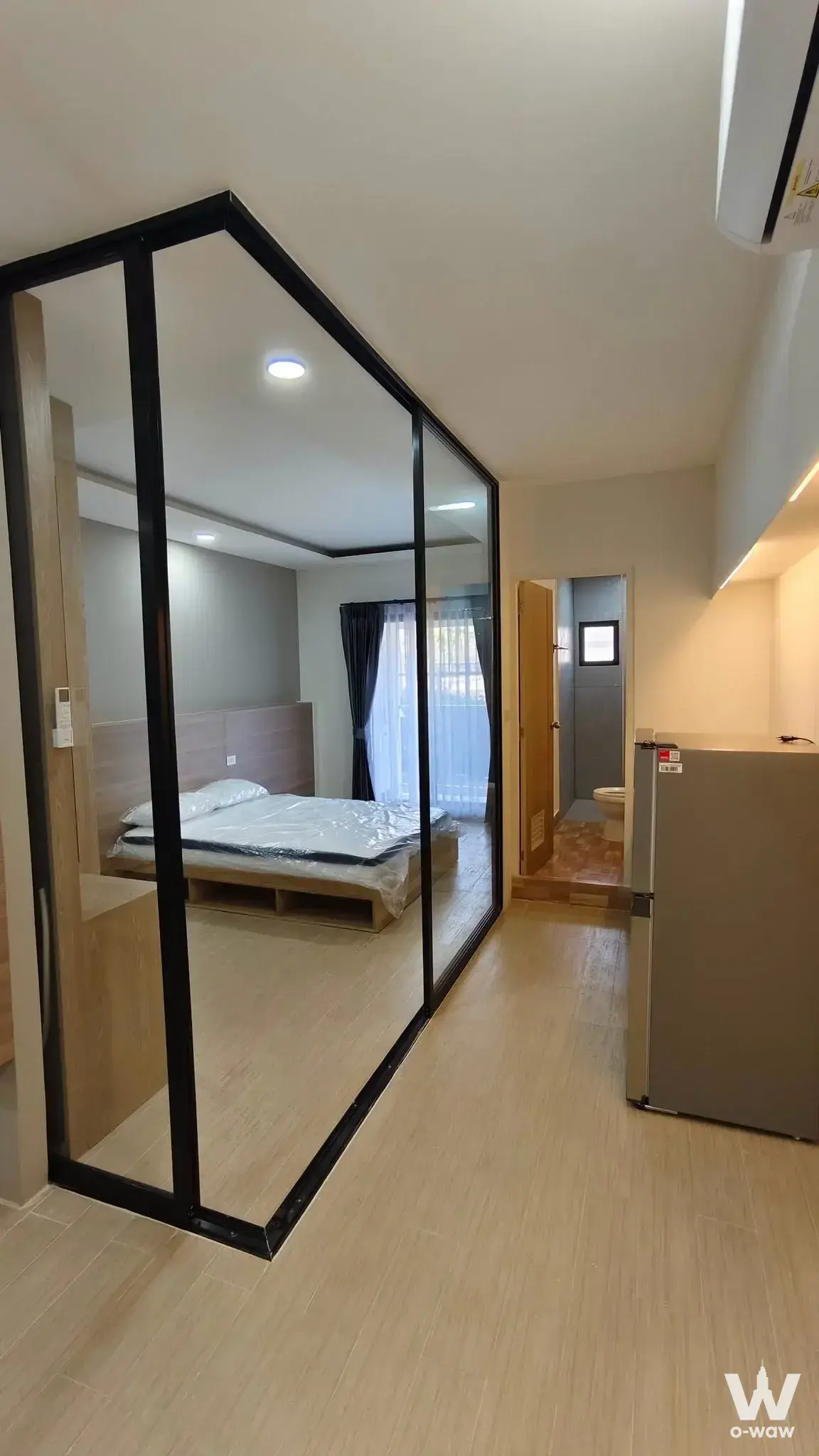 Studio apartment in Level Bangna featuring glass partition, plastic-wrapped bed, and kitchenette