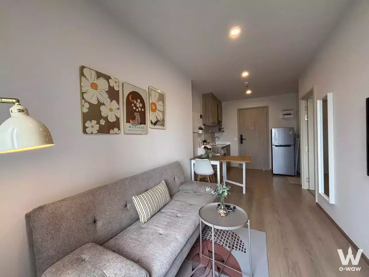 Open-plan studio with grey sofa, dining table, and full-length mirror in Life Rama 4 Asoke condo