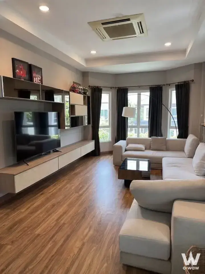 Modern living room in Grand Bangkok Boulevard house with L-shaped sofa, glass coffee table, and floor-to-ceiling windows