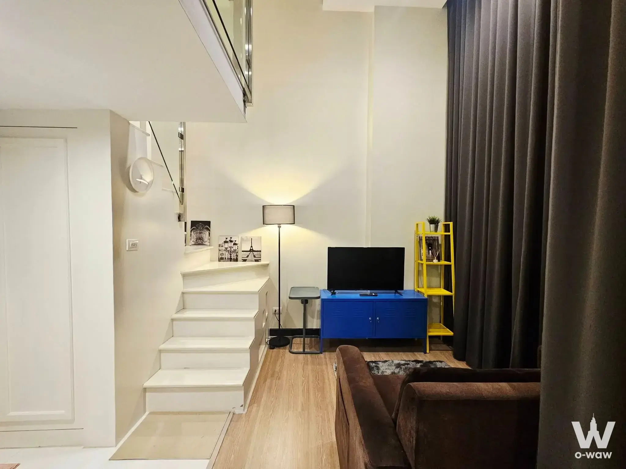 Loft living room in a 1-bed Thames Residence condo has a glass-railed staircase and a bright blue media console