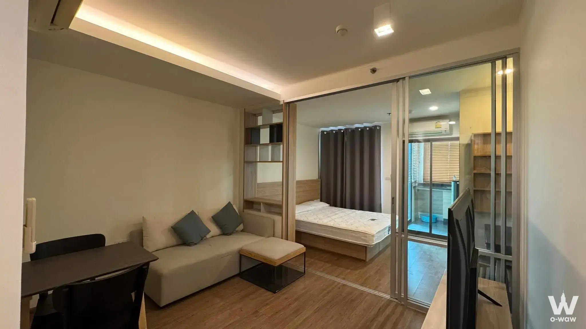 Modern studio in U Delight Residence with glass-partitioned bedroom, beige sofa, dining set, and light wood laminate floors